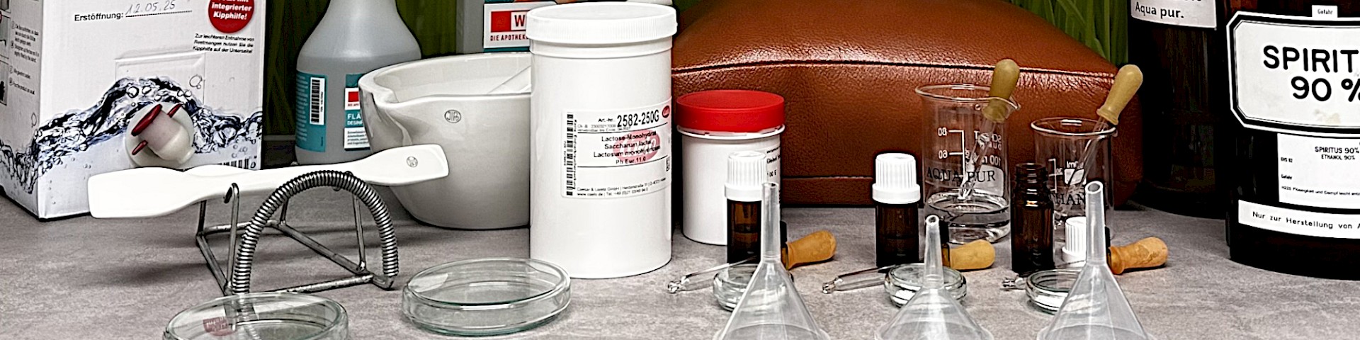 Utensilien zur Herstellung homöopathischer Arzneien (Messlöffel, Milchzucker, Flaschen und Dosen mit diversen Ausgangssubstanzen, Arzneifläschchen, etc. auf einem Tisch)