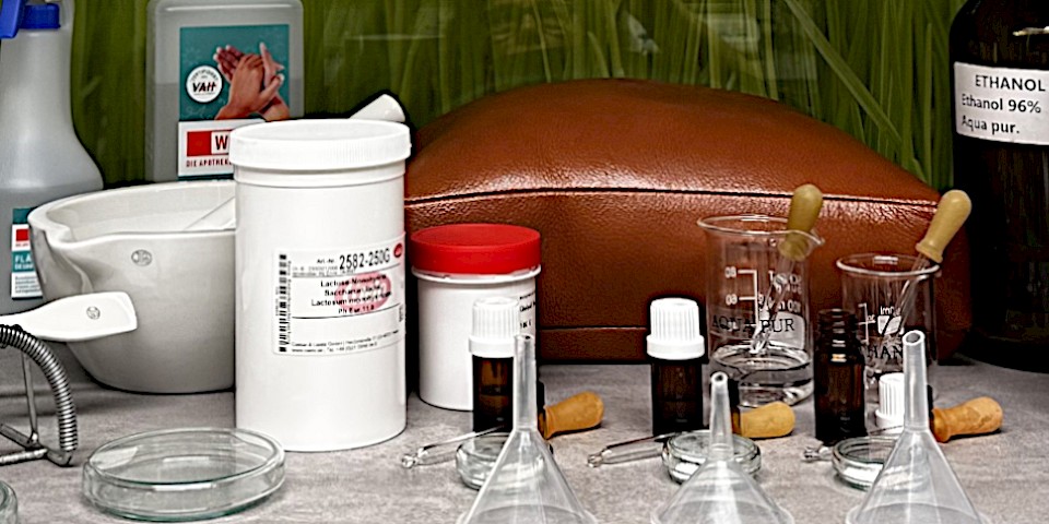 Utensilien zur Herstellung homöopathischer Arzneien (Messlöffel, Milchzucker, Flaschen und Dosen mit diversen Ausgangssubstanzen, Arzneifläschchen, etc. auf einem Tisch)
