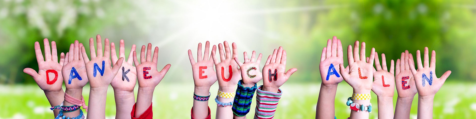 Viele Hände zeigen nach oben, die Handflächen mit Buchstaben bemalt bilde sie zusammen die Worte: Danke Euch allen.