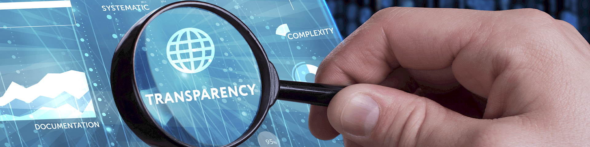 Hand with magnifying glass examining the value ‘Transparency’ on a digital screen display – symbolic of scientific work and transparency