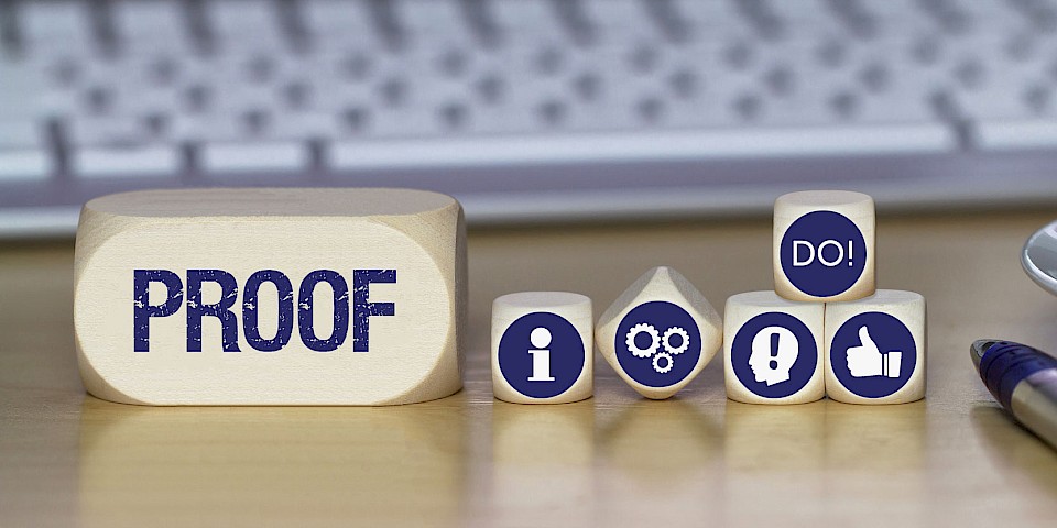 Auf einem Schreibtisch liegen mehrere Holzwürfel mit Symbolen, die den Prozess der evidenzbasierten Medizin darstellen: „Proof“ für Nachweis, „Information“, Zahnräder für die Evidenzbewertung, ein Kopf mit Ausrufezeichen für Erkenntnis sowie ein Daumen hoch, über dem ein Würfel mit der Aufschrift „DO“ die Umsetzung symbolisiert.