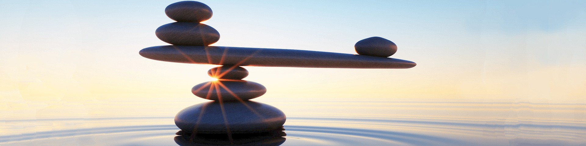 Ausbalancierte aufeinandergestapelte Steine bei Sonnenaufgang im Meer.