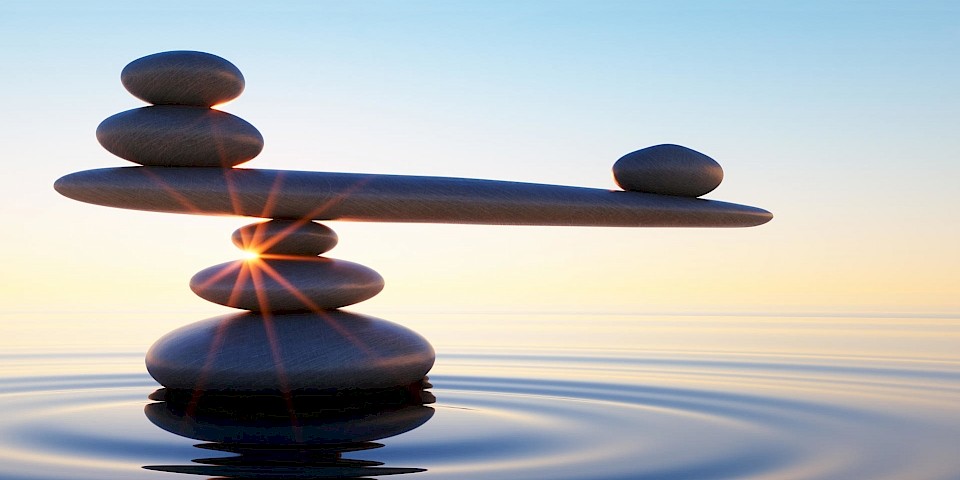 Ausbalancierte aufeinandergestapelte Steine bei Sonnenaufgang im Meer.