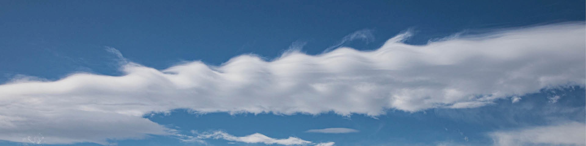 Weiter Ausschnitt des blauen Himmels mit verschiedenen Wolkenformationen und -ebenen, die eine vielschichtige Struktur erkennen lassen.