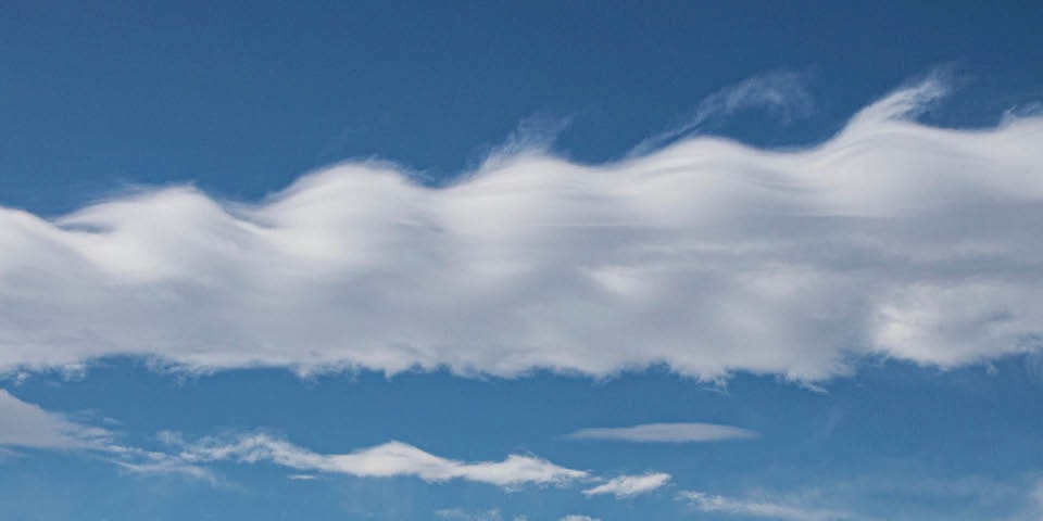 Weiter Ausschnitt des blauen Himmels mit verschiedenen Wolkenformationen und -ebenen, die eine vielschichtige Struktur erkennen lassen.