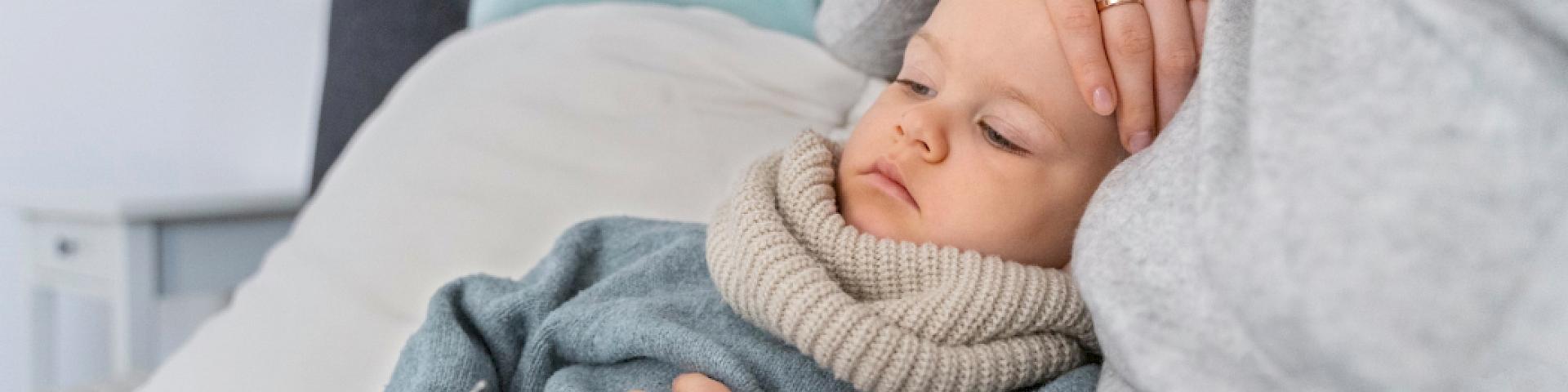 A mother lovingly holds her feverish toddler in her arms. A moment full of care, closeness and security.