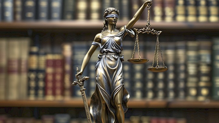Lady Justice statue holding scales of justice, symbolizing legal integrity and fairness, with background shelves of antique books in a library.